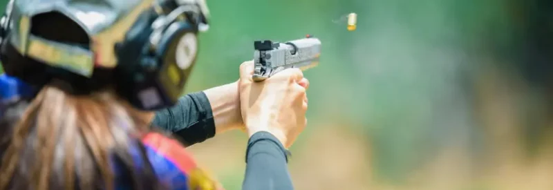 A person with a hat and headphones holding a pistol sold with a New Mexico FFL.