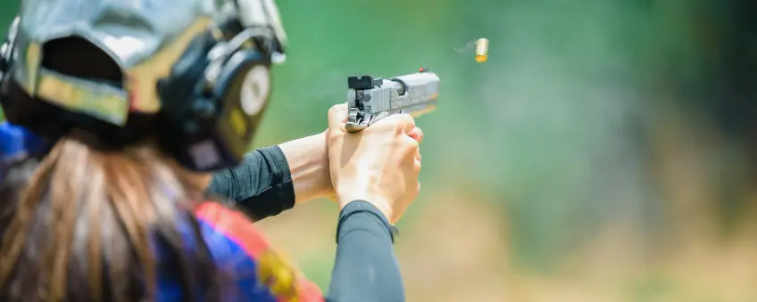 A person with a hat and headphones holding a pistol sold with a New Mexico FFL.