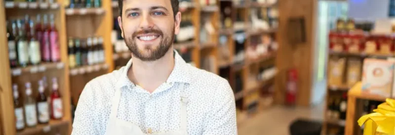 A smiling man standing in front of shelves of alcohol sold with a Texas liquor license.