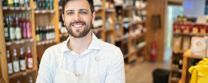 A smiling man standing in front of shelves of alcohol sold with a Texas liquor license.