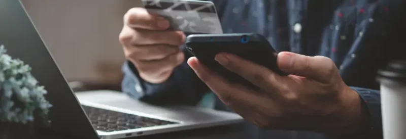 Business owner with cell phone, credit card, and laptop getting set up with Worldpay merchant services.