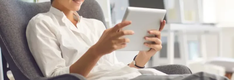 A woman looking at her iPad in an armchair, preparing to cancel a subscription through click-to-cancel.