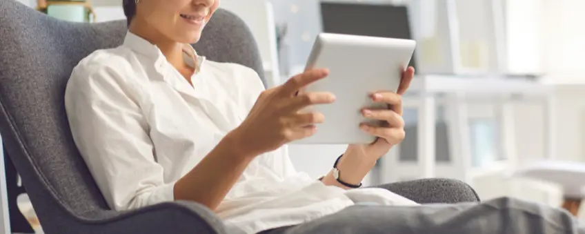 A woman looking at her iPad in an armchair, preparing to cancel a subscription through click-to-cancel.