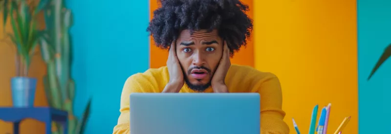 A guy looking at his laptop, shocked and frustrated.