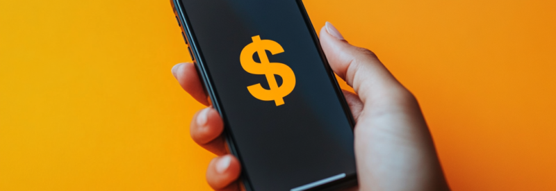 Hand holding a smartphone displaying a dollar sign on an orange background.