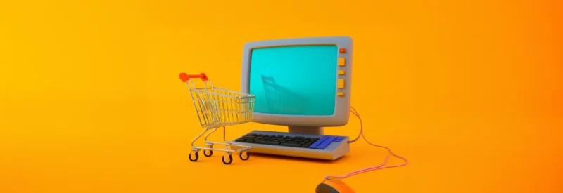 Miniature shopping cart next to a vintage computer on an orange background.