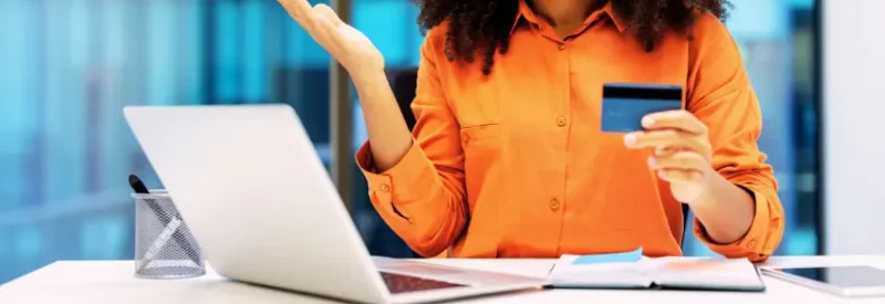 Travel agency merchant holding up credit card in front of laptop dealing with fraud