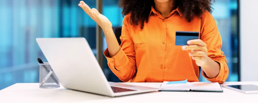 Travel agency merchant holding up credit card in front of laptop dealing with fraud